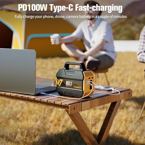 Portable charger on a table with a laptop and people camping in the background.
